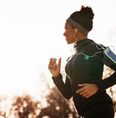 Happy African American woman with earphones running in the park.